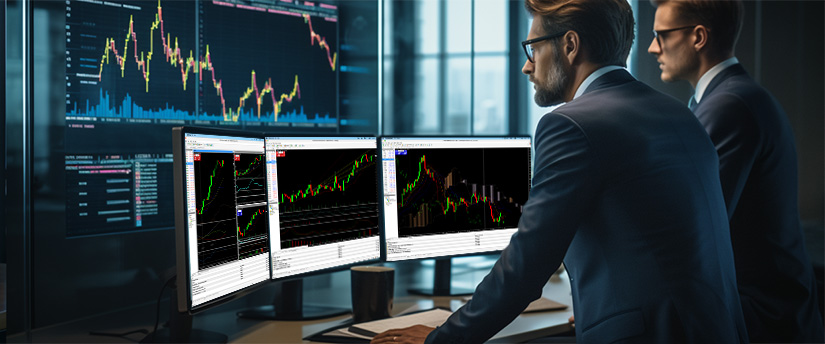 Two men in suits analyze trading data displayed on a computer screen in a professional setting.
