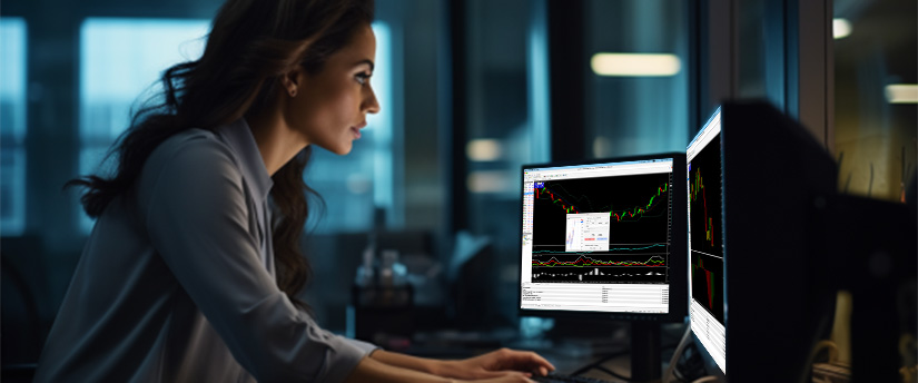 Una mujer sentada en un escritorio, trabajando en dos monitores de computadora, concentrada en sus tareas.