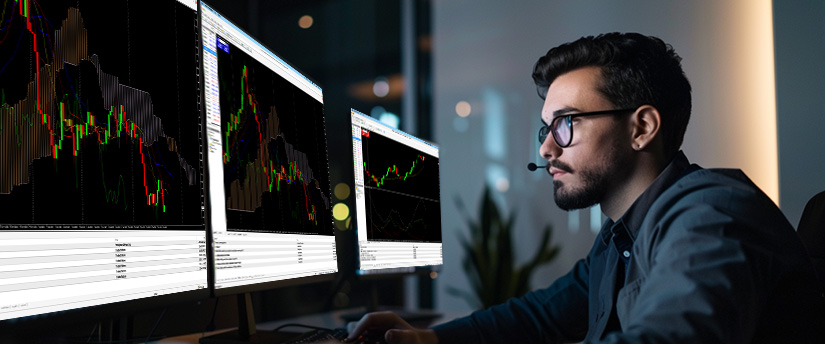 A man wearing glasses intently observes a computer screen displaying CFD trading data.