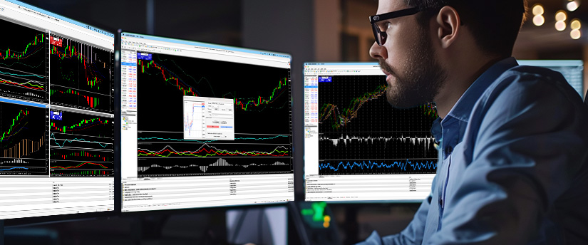 A man at a desk with multiple screens displaying various trading platforms and market data.