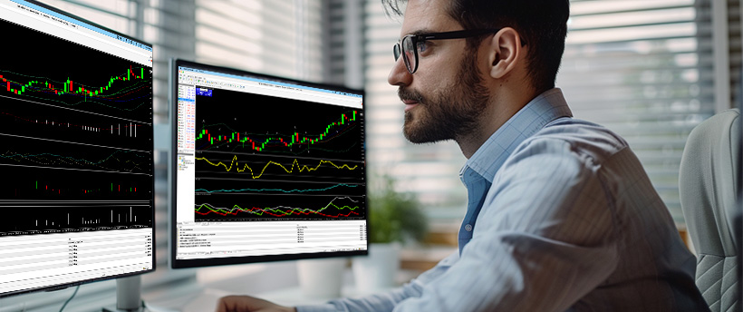  Un homme portant des lunettes analyse des données de trading forex affichées sur deux écrans d’ordinateur