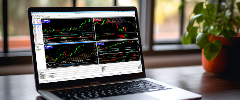 A laptop open on a wooden desk next to a potted plant, displaying four trading chart windows with market data and AI signals.